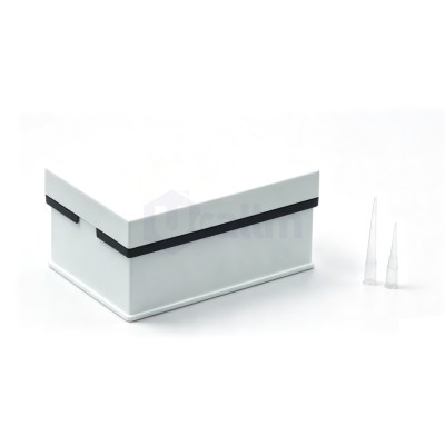 White rectangular box with a light gray lid and black trim sits on a white surface; three clear plastic tubes or vials stand to the right.